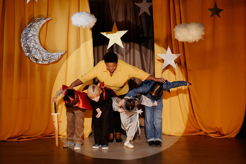 Children Performing On Stage with Teacher Guiding